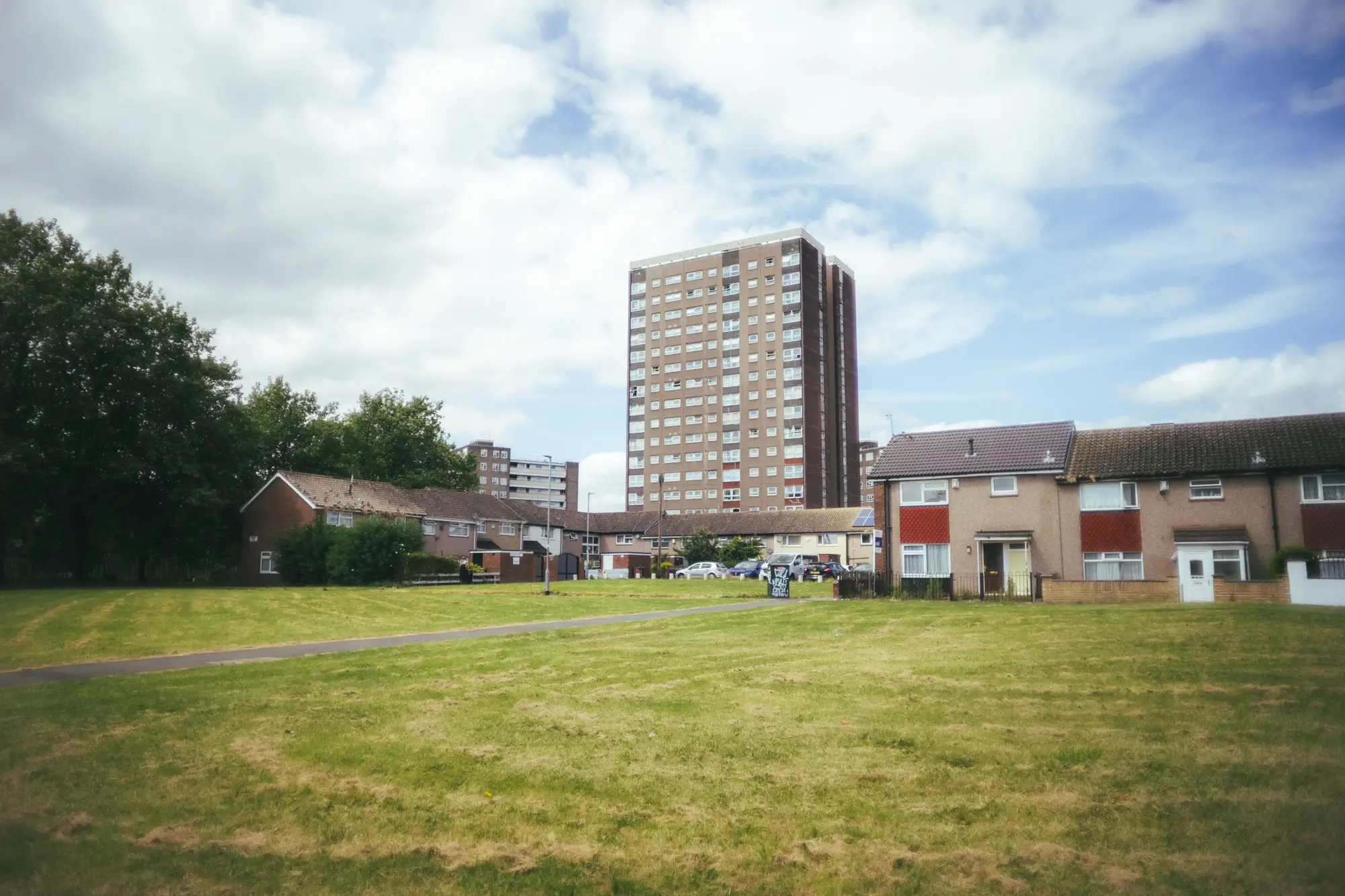 A council estate in Leeds on a summer day: low-rise brick houses, a tower block and an open stretch of mown grass